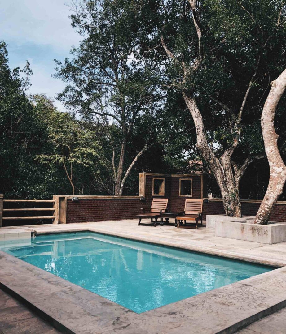 a swimming pool with two chairs and trees
